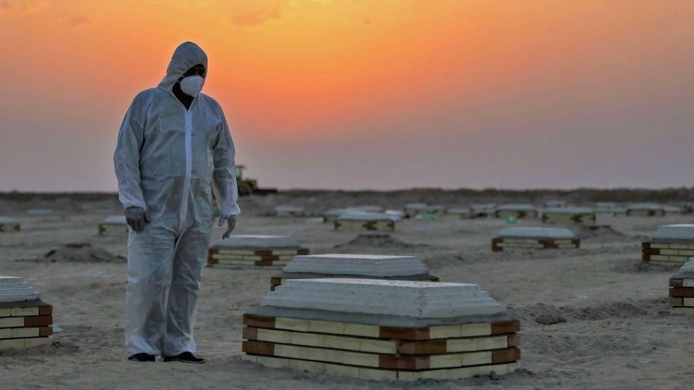 A masked grave digger observers the graves in a cemetery in Iraq