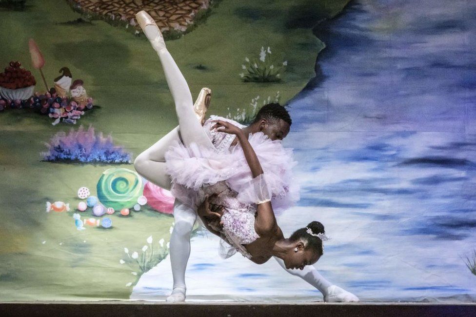 A male and female ballet dancer perform a complex lift on stage.