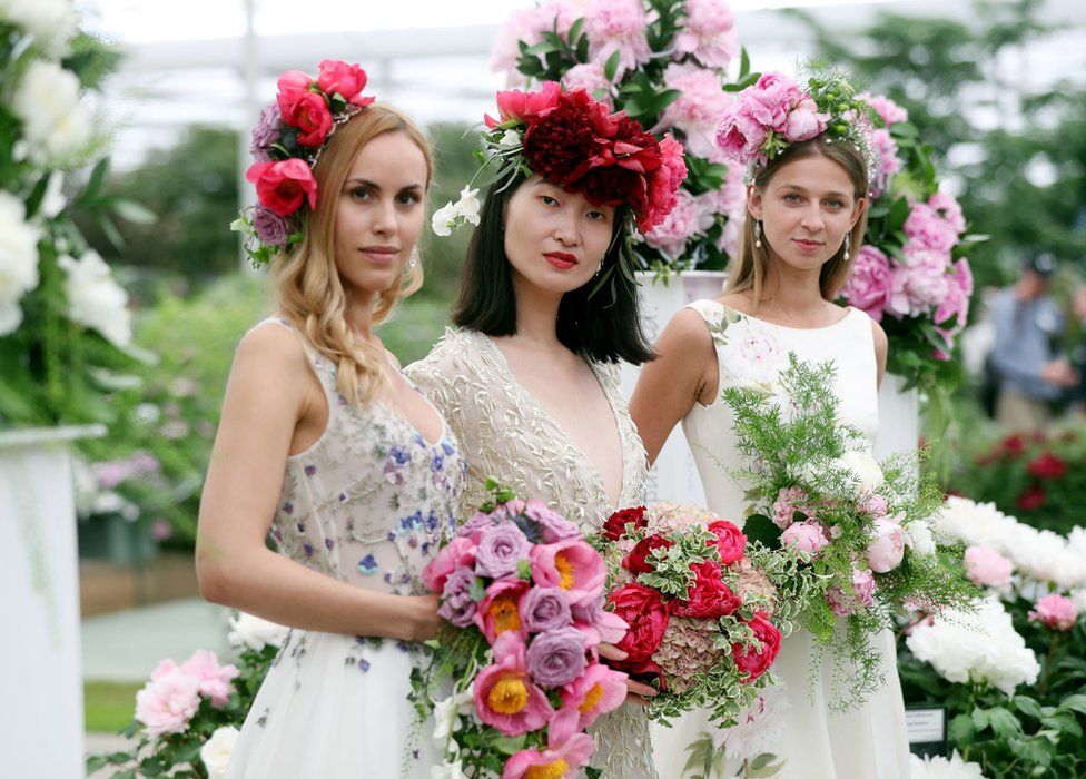 Three models wearing bridal designs by Alan Hannah hold bouquets of peonies in the Great Pavilion during the press day for this year's RHS Chelsea Flower Show