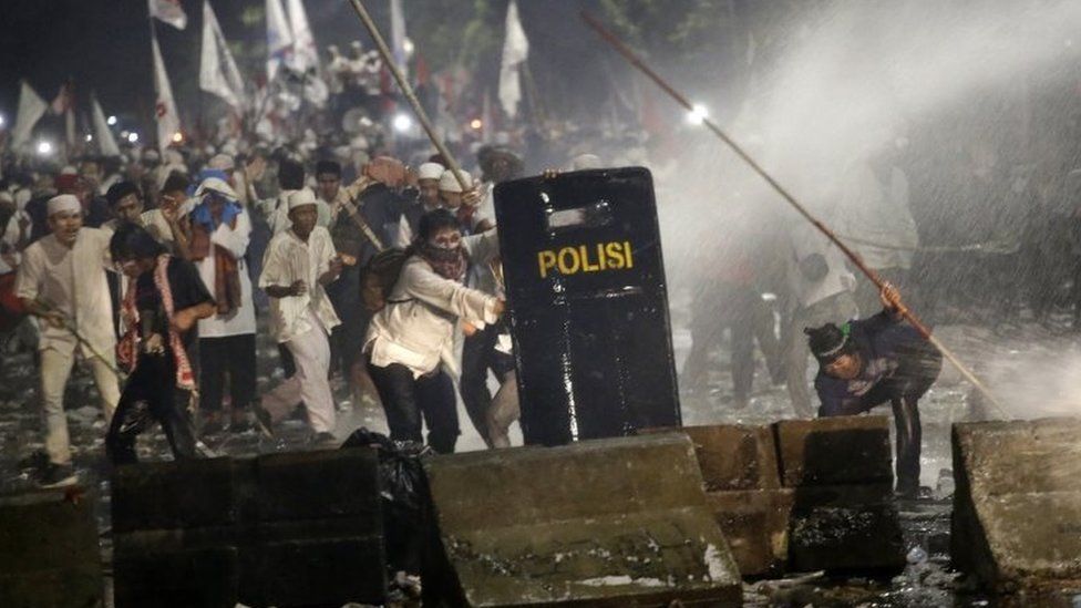 Protesters are sprayed with water from a police water cannon truck during a clash outside the presidential palace in Jakarta, Indonesia, Friday, Nov. 4, 2016