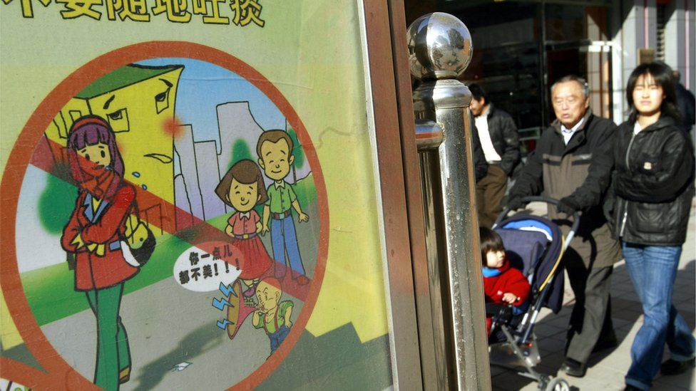 Pedestrians walk past a signboard reading 'please do not spit and others social ills', on display along a street in Beijing, 17 November 2007, ahead of the 2008 Olympics.