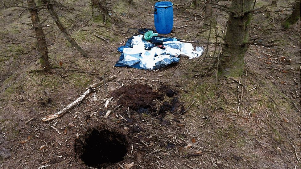 A hole in the ground in the forest with the weapon that had been stored inside