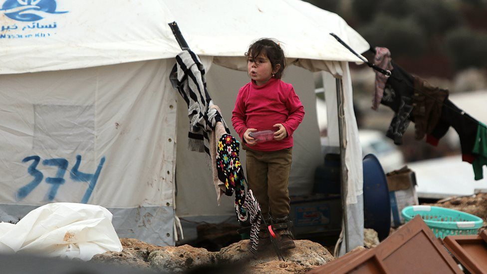 A Syrian girl walks past a tent at a makeshift displacement camp in Idlib province, Syria (18 February 2020)
