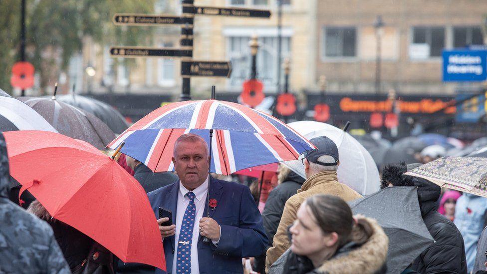 People holding umbrellas, including one in union jack colours as well as plain ones. Shops in The Drapery in Northampton are visible in the background