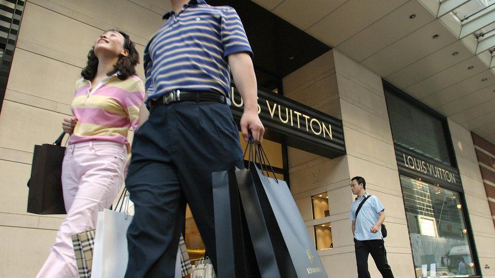 Chinese shoppers walk past a Louis Vuitton store