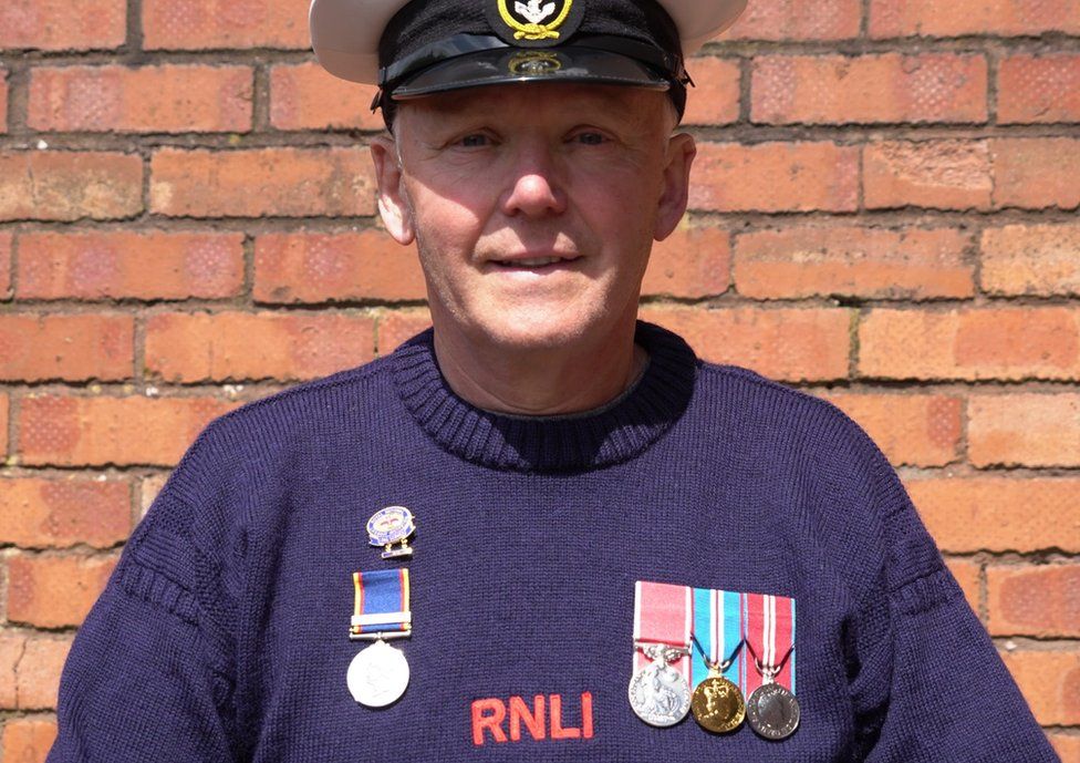 A man in a blue jumper, RNLI hat and medals