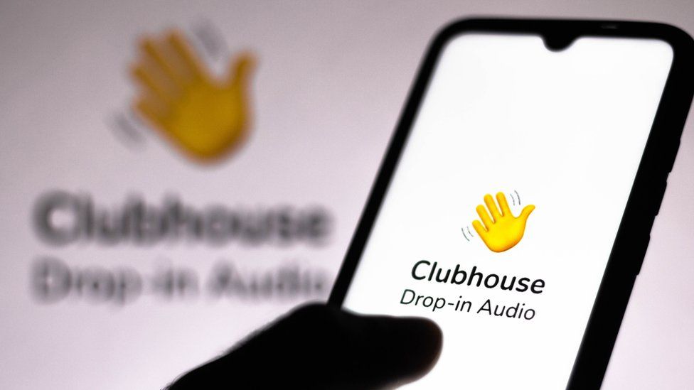 The Clubhouse logo is seen on a smartphone being held by a hand in this close-up shot