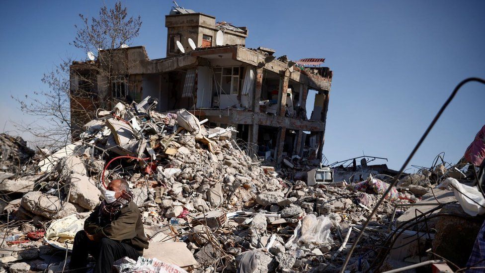 A man sits among rubble in the aftermath of a deadly earthquake in Kahramanmaras, Turkey