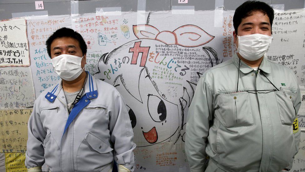 Two workers stand in front of a wall of messages of support
