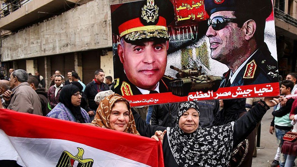Egyptian women hold their national flag and a poster bearing portraits of President Abdul Fattah al-Sisi (R) and Defence Minister Sedki Sobhi in Tahrir Square, on the sixth anniversary of the 2011 uprising that ousted Hosni Mubarak (25 January 2017)