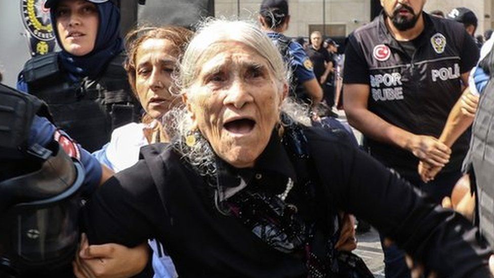 An elderly female demonstrator is detained by police