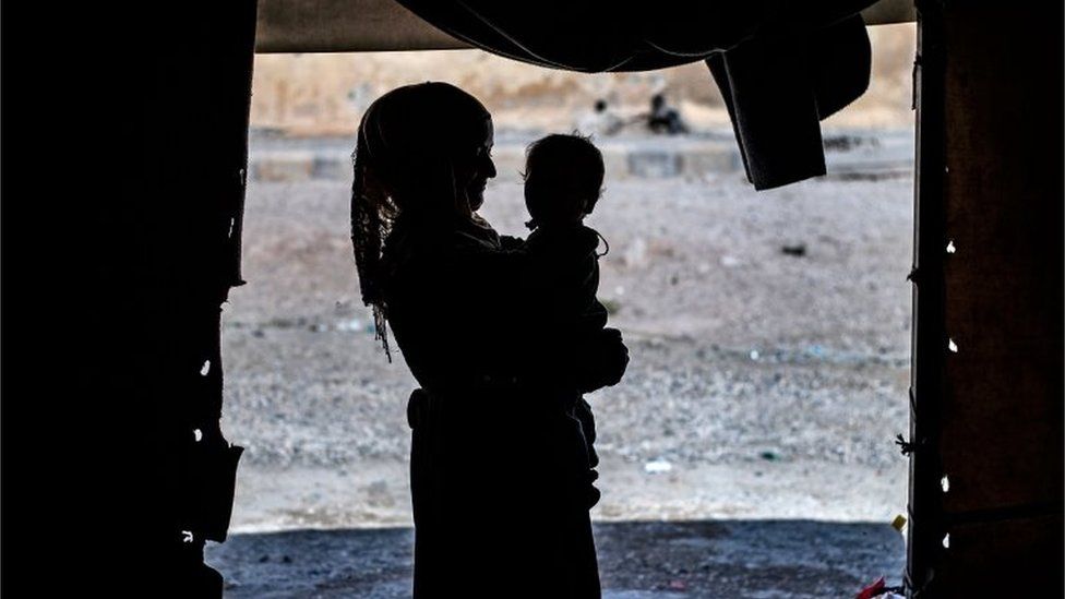 A volunteer caretaker holding one of 24 orphaned children is silhouetted at a camp in the northern Syrian village of Ain Issa, on 26 September 2019.