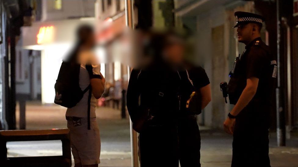 Teenagers with blurred out faces talking to police officers in a street in Ipswich at night