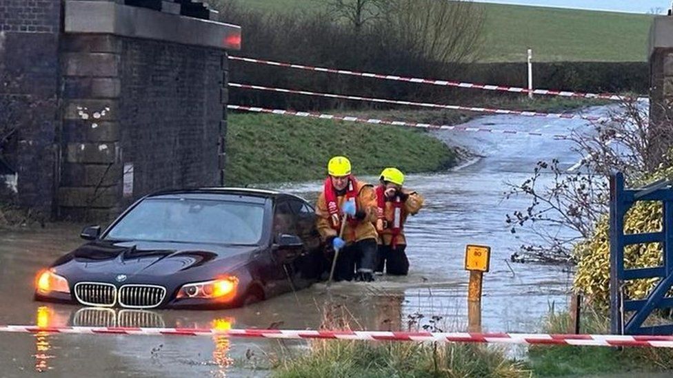 Firefighters rescuing man from car in flood water