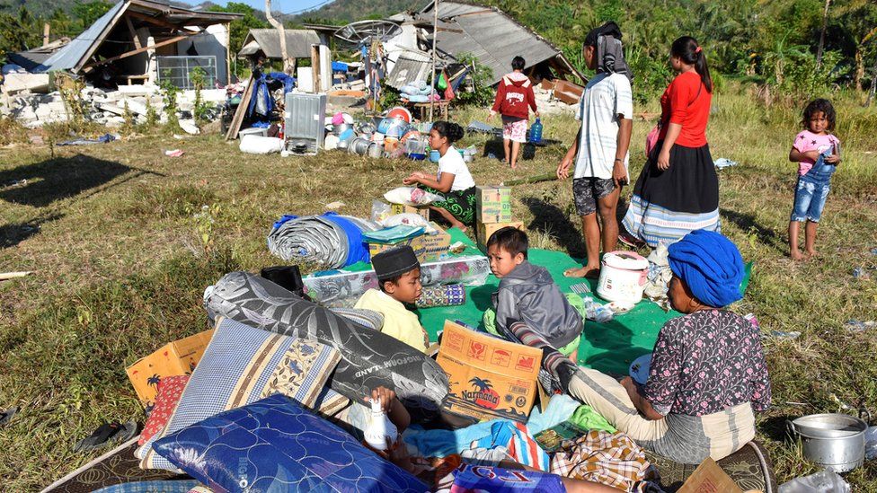 Residents sit outside their home with their belongings following a strong earthquake in Pemenang, North Lombok