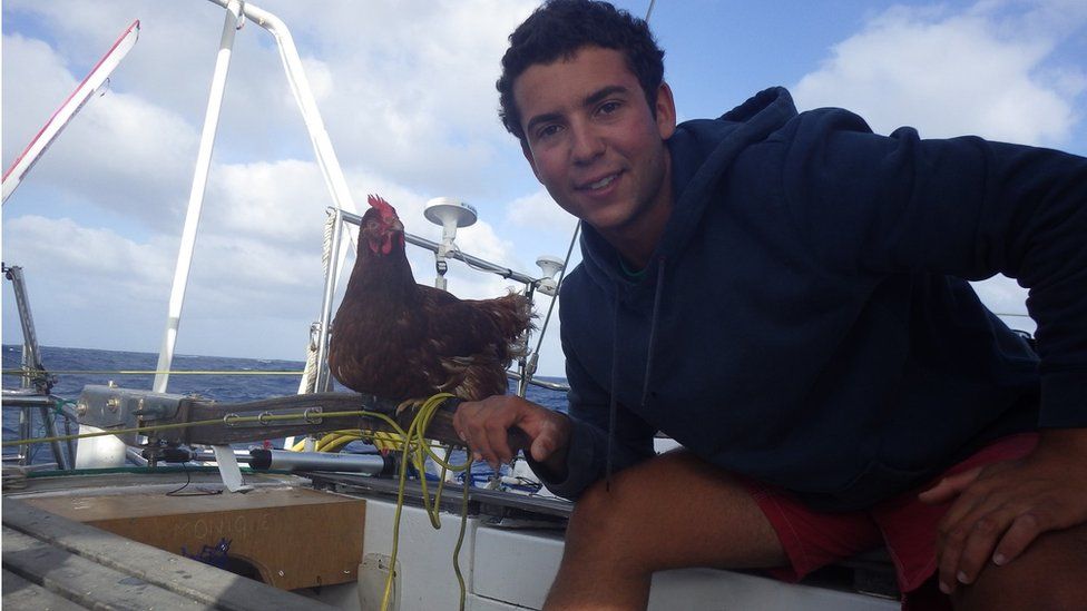 Sailor Guirec Soudee holding his hen Monique on the deck of a yacht