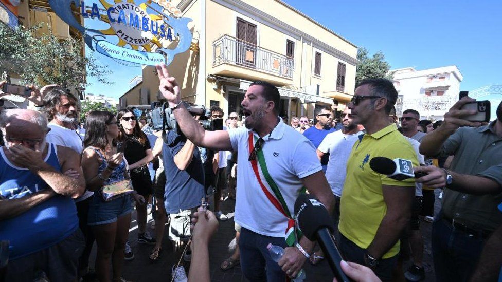 Вице-мэр Лампедузы Аттилио Люсия (в центре) и группа граждан блокируют улицу Виа Витторио Эмануэле и прерывают движение транспорта, протестуя против миграционной политики в Лампедузе, Италия, 16 сентября 2023 года.