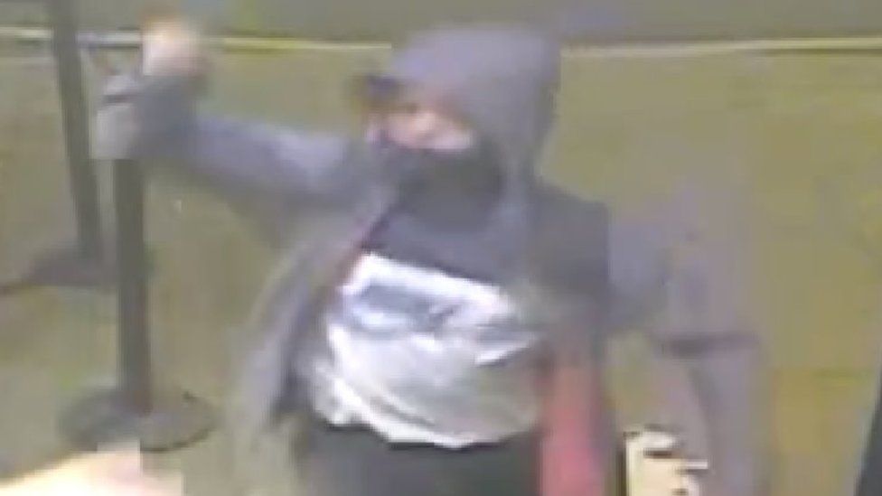 CCTV image showing a man wearing a dark hooded coat, face covering and black and white top.
