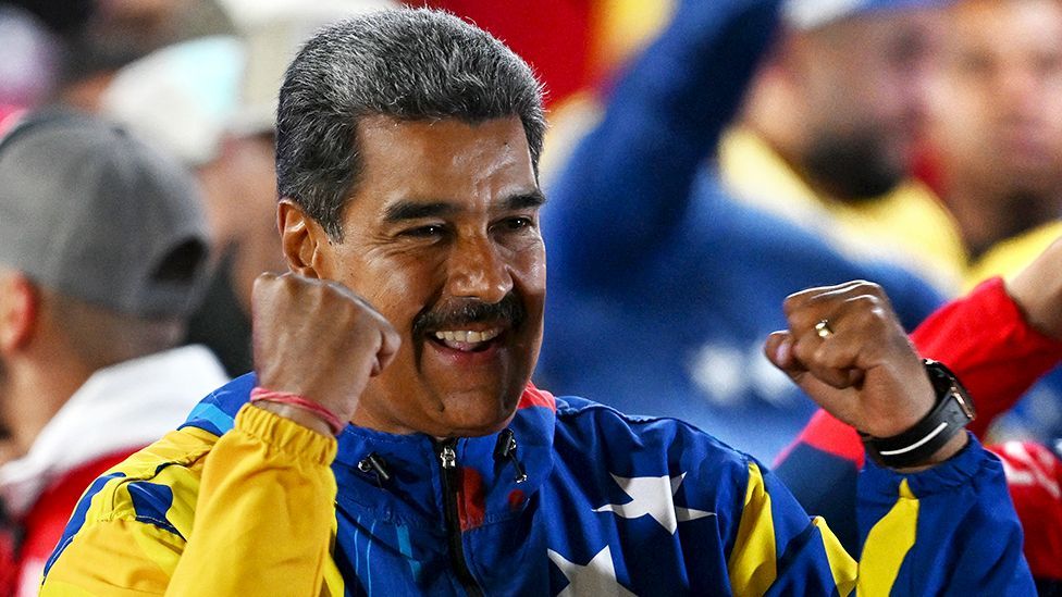 Venezuelan President Nicolas Maduro smiles and raises his fists to celebrate in a blue and yellow top on 29 July