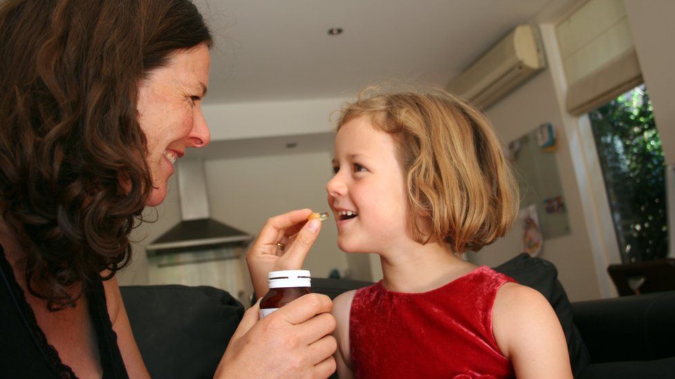 mum giving daughter a vitamin tablet