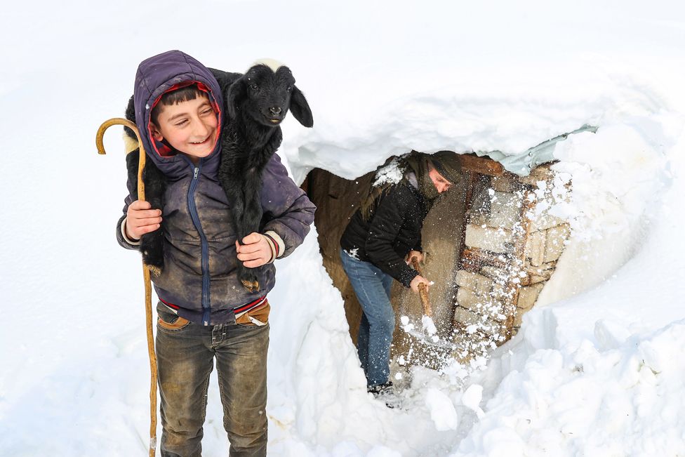A boy carrying a goat is seen in a snow-covered field in front of his house, in Van, Turkey