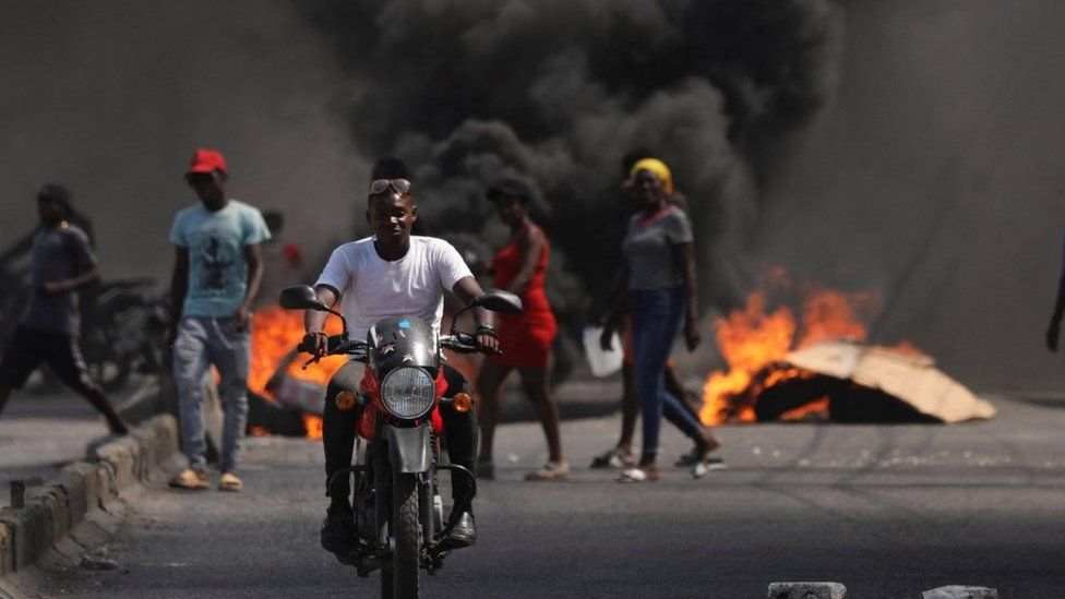 A man rides past a burning barricade during a protest against Prime Minister Ariel Henry's government