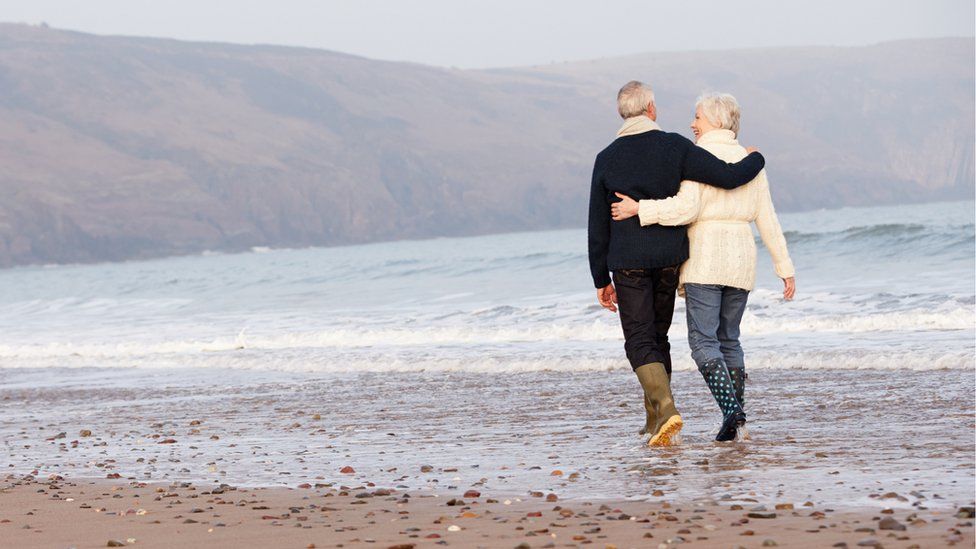 retired couple walk on a beach