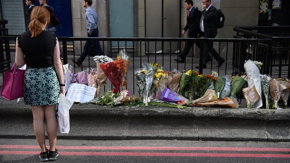 A commuter looks at some of the floral tributes on London Bridge