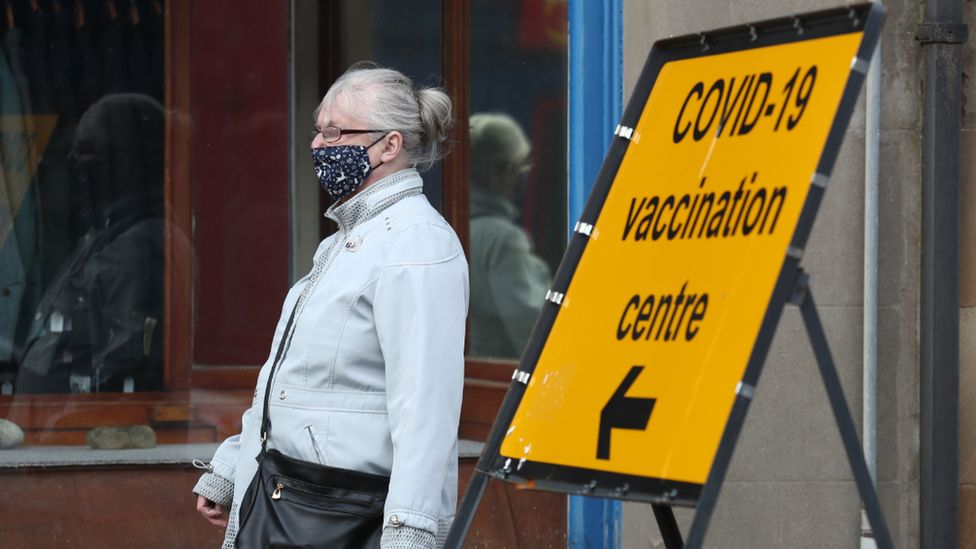 Masked woman walks past Covid sign
