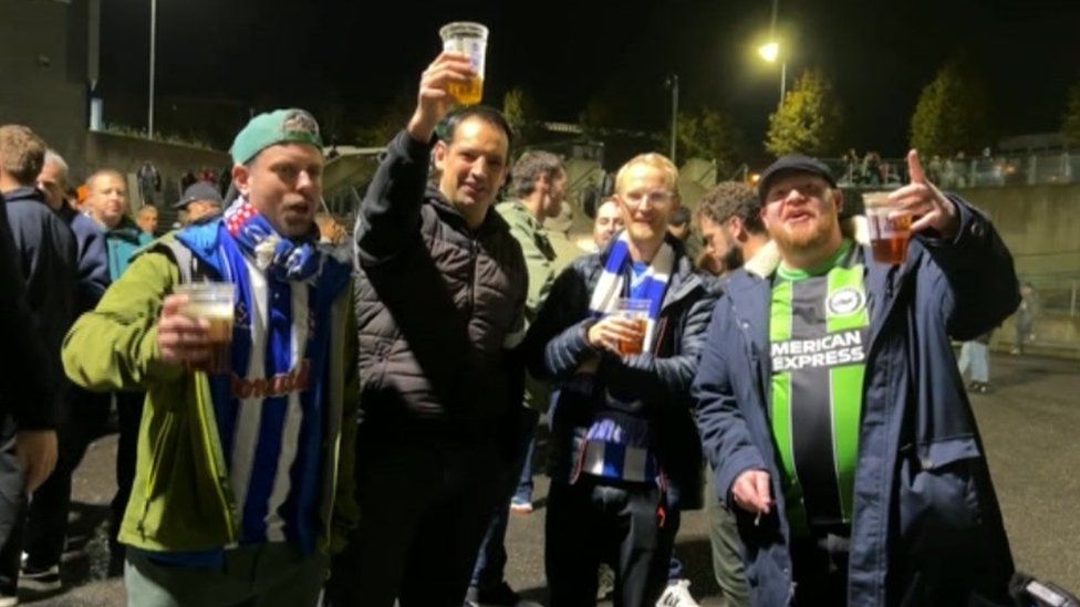Four Albion fans wearing Seagulls scarves and raising a pint after the match