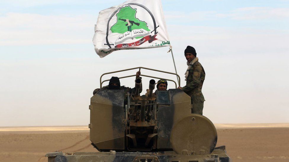 Fighters stand in the turret of an infantry fighting vehicle flying the flag of one of the units of the Popular Mobilisation Units as they advance with Iraqi forces through Anbar province, on November 25, 2017