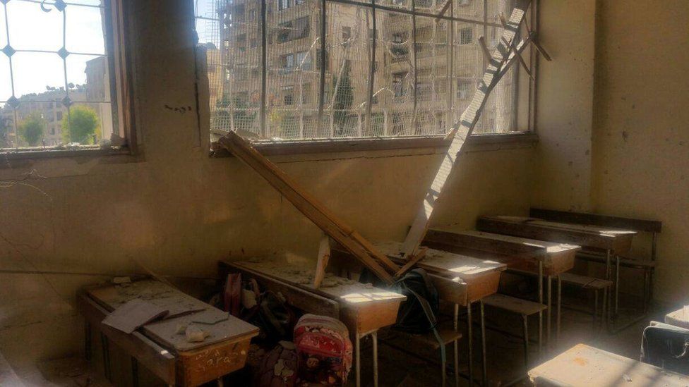 A damaged classroom with dust-covered desks