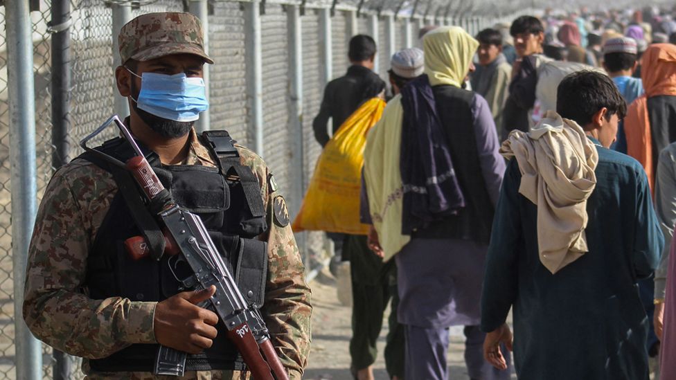 A Pakistani soldier stands guard as Afghans walk along fences after arriving in Pakistan through the Pakistan-Afghanistan border crossing point in Chaman on 26 August 2021