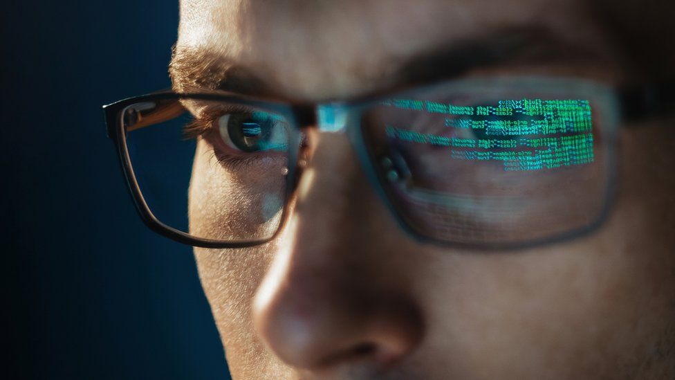 A stock image of someone looking at a screen with code reflected in their glasses