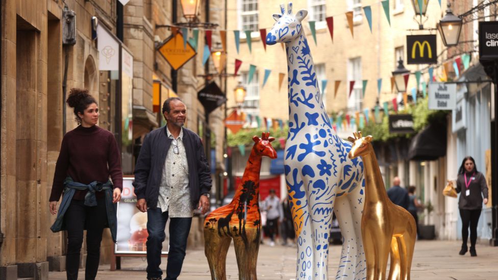 Two passers-by looking at a giraffe sculpture