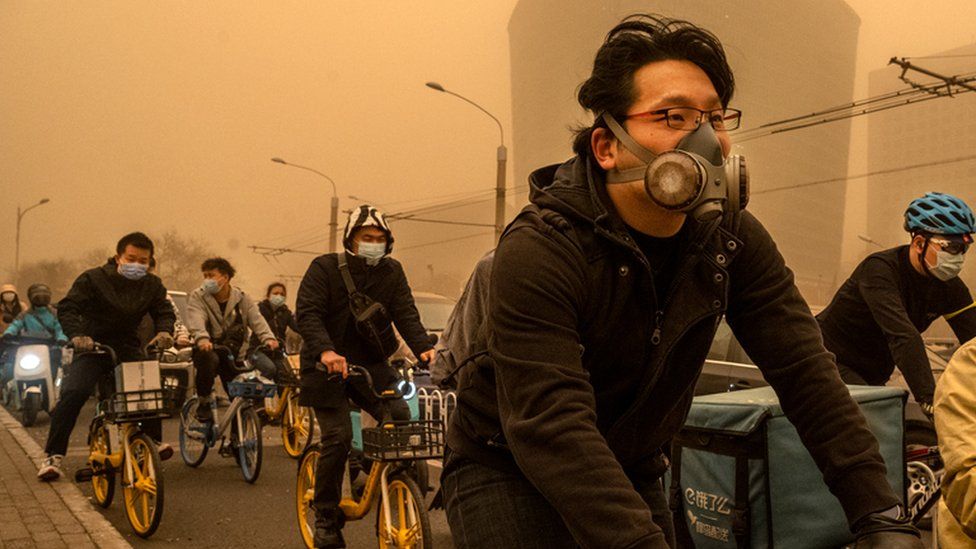 People wear protective masks as they cycle during a sandstorm on 15 March 2021 in Beijing