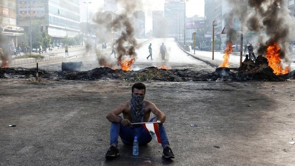 A protester sits in front of flames in Dora, Lebanon