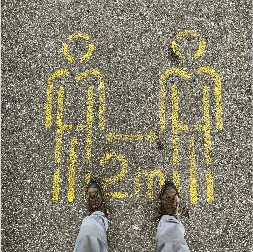 A stencil outline on the ground instructing social distancing