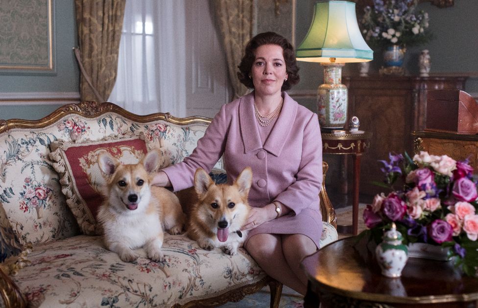 Actress Olivia Colman in character as Queen Elizabeth II in Netflix show The Crown, pictured on a sofa with two Corgis