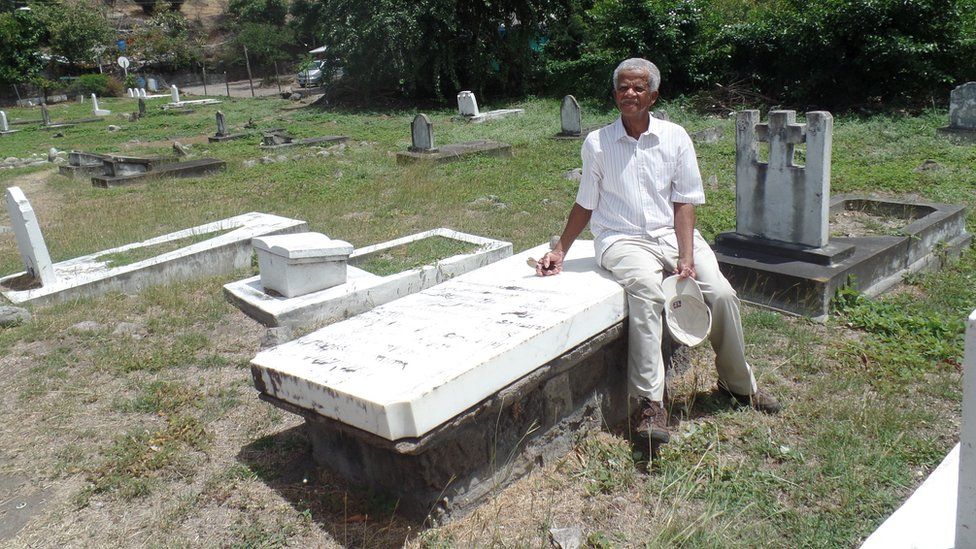 Joe Sweeney sits on the grave where his ancestor is buried in Montserrat's Carr Bay cemetery