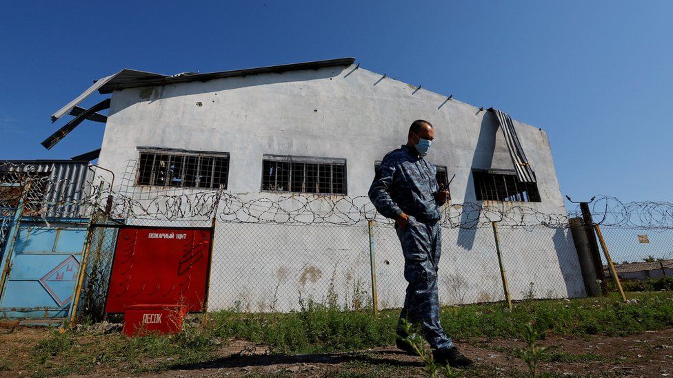 A security guard stands outside a building at Olenivka prison camp after it was damaged by shelling in July