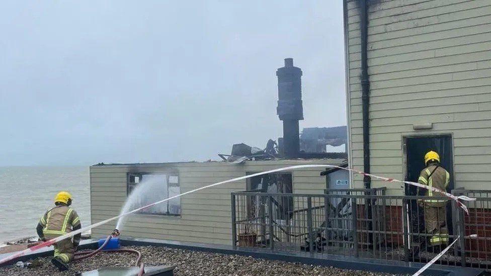 Two firefighters behind fluttering emergency service s tape with water from a hose spraying into a window