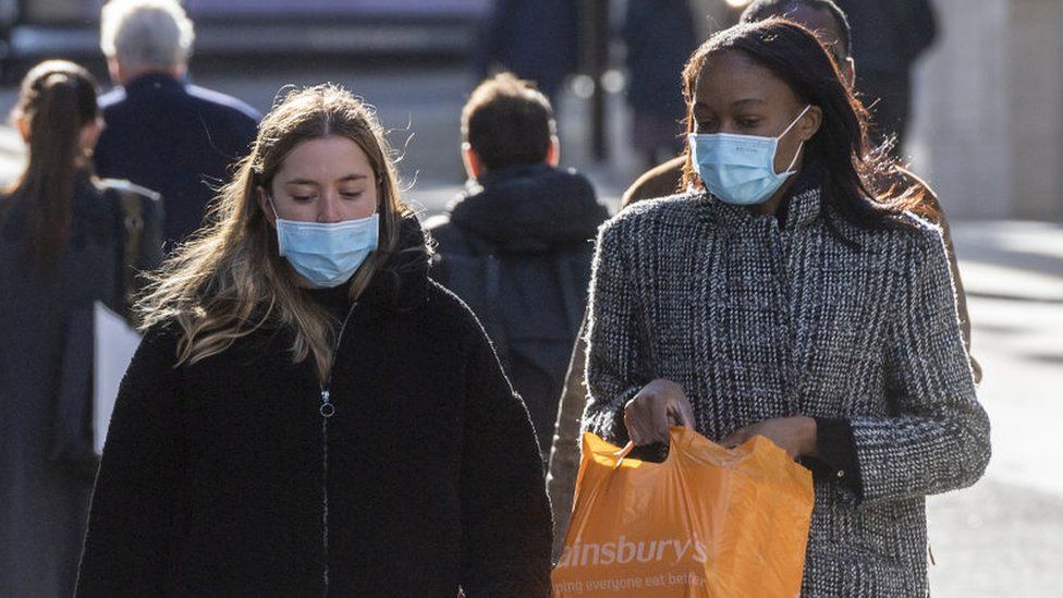 Two women wearing face mask walk along a street in London
