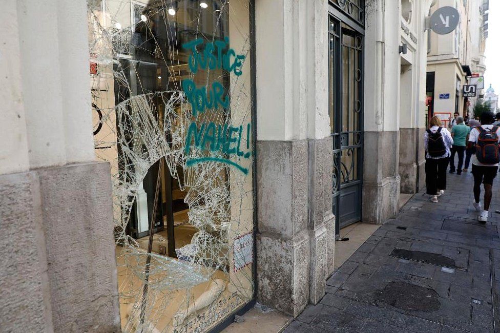 People walk past a damaged shop following a night of looting and rioting in Marseille on 1 July 2023