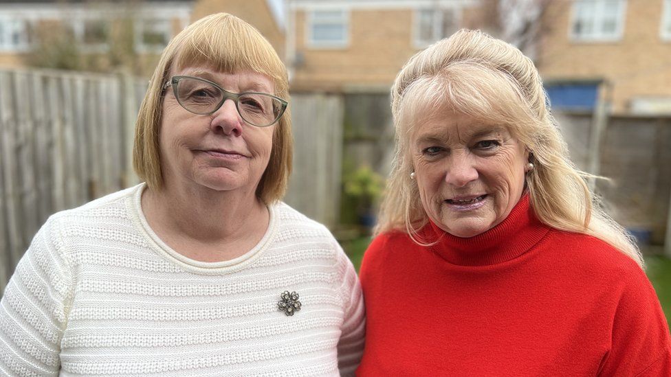 Yvonne Mitchell, wearing a white jumper, and Val Thomas, wearing a red polo neck, standing side by side in the garden of The Sandfield