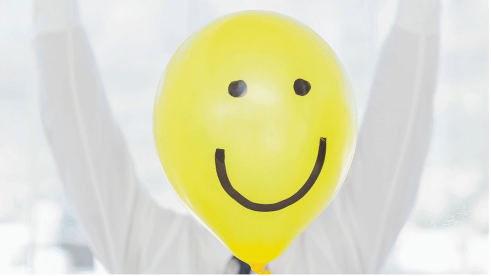 Man with happy face balloon in front of his face