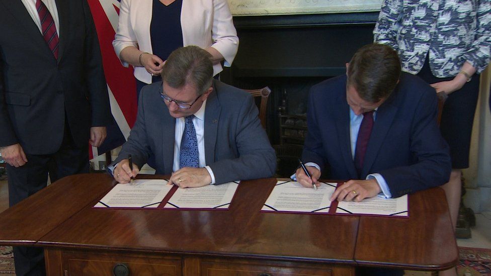 The DUP's Sir Jeffrey Donaldson and Gavin Williamson of the Conservative Party sign a deal in Downing Street