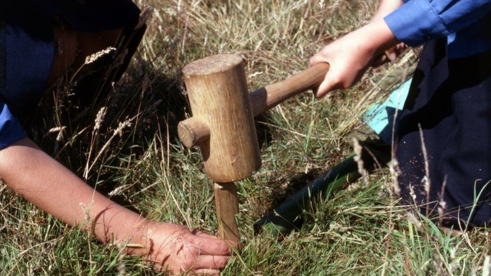girl guides hammer a tent peg into the ground