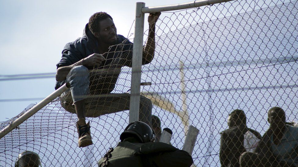 African migrants sit on top of a border fence during an attempt to cross into Spanish territories, between Morocco and Spain's north African enclave of Melilla, on 21 November 2015.
