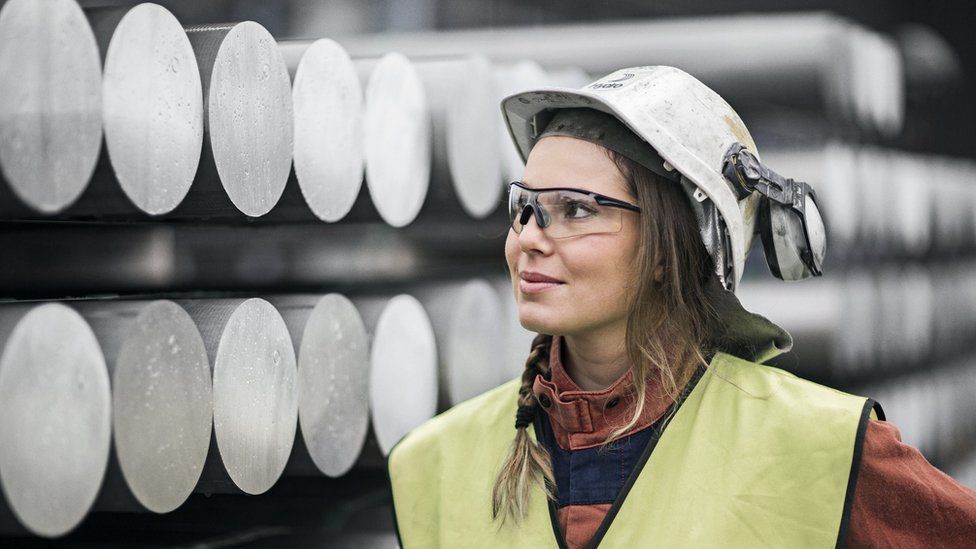 Female Norsk Hydro worker standing in front of aluminium tubes
